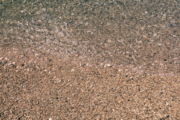 Stones under water. Sea pebbles on the beach. Sea pebbles on the beach sand with transparent water. Natural sea stones closeup. Beach smooth pebbles. Tourism and travel themed. Vacation background.