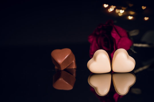 Heart shaped chocolates and red rose on black background