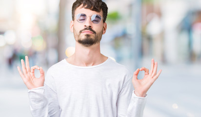 Young handsome man wearing sunglasses over isolated background relax and smiling with eyes closed doing meditation gesture with fingers. Yoga concept.