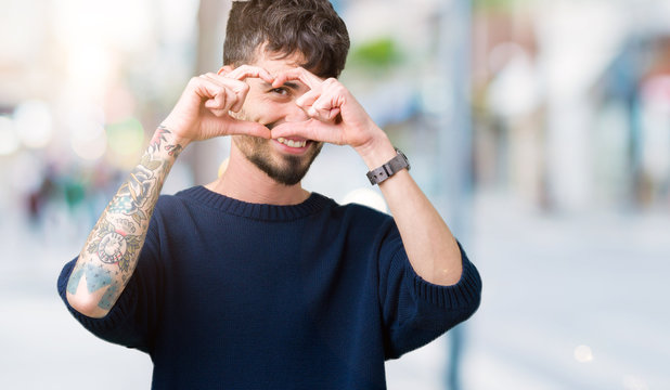 Young handsome man over isolated background Doing heart shape with hand and fingers smiling looking through sign