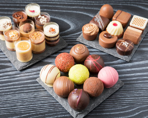 Sweet dessert, filled chocolates - Close up of delicious chocolate pralines beautifully arranged on a black wooden table