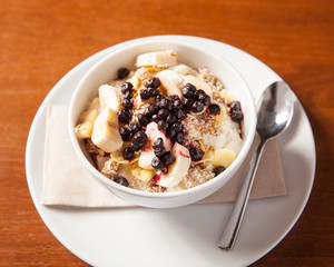 Healthy cereal breakfast bowl - oat porridge with fruits, beautifully arranged in a green bowl on a wooden table