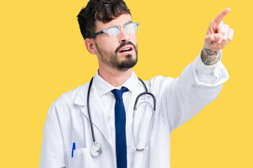 Young doctor man wearing hospital coat over isolated background Pointing with finger surprised ahead, open mouth amazed expression, something in front
