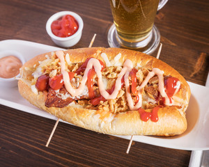 American food, Hot Dog - Delicious hot dog with sauces, served on a wooden table with a beer