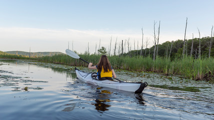 woman paddling across a calm lake in a white kayak