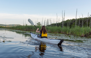 woman paddling on calm lake inside of a white kayak