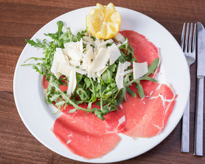 Delicious Italian food - Top view of fresh carpaccio, beautifully arranged on a white plate on a wooden table