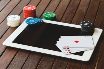 Close-up top view of chips, dices and cards on a tablet. Poker online concept.