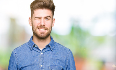 Young handsome blond man wearing casual denim shirt winking looking at the camera with sexy...
