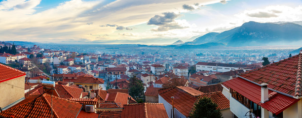 Greek town evening panorama with red roof houses in the valley with sunset mountains, Kalabaka,...