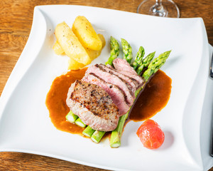 Close up, top view of filet steaks with asparagus and potatoes, beautifully arranged and served on a dark wooden table