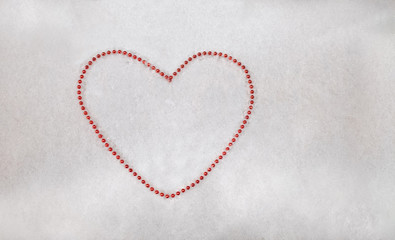 A heart laid out of beads on a background of white snow with space for text.