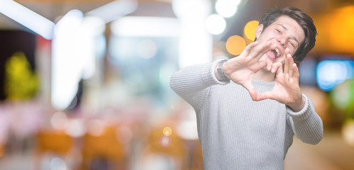 Young handsome man wearing winter sweater over isolated background smiling in love showing heart symbol and shape with hands. Romantic concept.