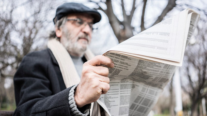 Naklejka premium Old man reading newspaper in the park