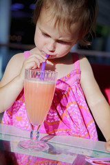 Little cute girl drinking tasty natural smoothie juice outdoors. Children's food, healthy lifestyle, vitamins concept.