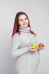 A pregnant woman is holding green and red apples.