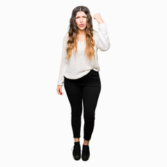 Obraz na płótnie Canvas Young beautiful woman wearing white sweater angry and mad raising fist frustrated and furious while shouting with anger. Rage and aggressive concept.