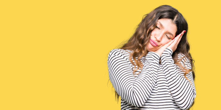 Young beautiful woman wearing stripes sweater sleeping tired dreaming and posing with hands together while smiling with closed eyes.
