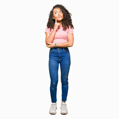 Young beautiful woman with curly hair wearing pink t-shirt with hand on chin thinking about question, pensive expression. Smiling with thoughtful face. Doubt concept.