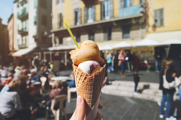 Woman's hand is holding Italian ice cream in waffle cone on blurred street background. Summer time or food concept. Selective focus.