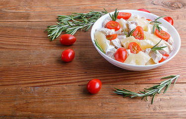 Chicken fillet salad with rosemary, pineapple and cherry tomatoes on brown wooden background.