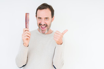 Senior man holding hair comb over isolated background pointing and showing with thumb up to the side with happy face smiling