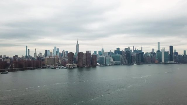 Aerial footage along the East River in New York City, between Brooklyn and Manhattan. Empire State Building and the UN General Assembly visible. Shot pans from Manhattan to Brooklyn, then descends.