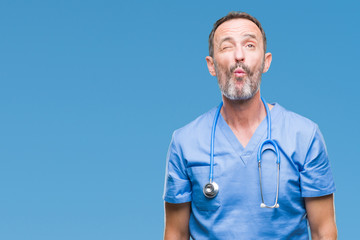 Middle age hoary senior doctor man wearing medical uniform over isolated background making fish...