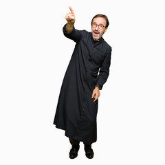 Middle age priest man wearing catholic robe Pointing with finger surprised ahead, open mouth amazed...