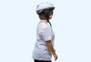 Young adult cyclist woman with down syndrome wearing safety helmet over isolated background looking to side, relax profile pose with natural face with confident smile.