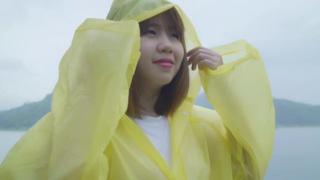 Slow motion - Young Asian woman feeling happy playing rain while wearing raincoat standing near lake. Lifestyle women enjoy and relax in rainy day.