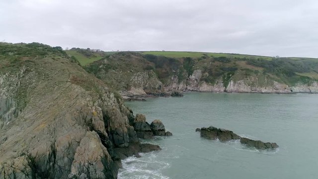 Aerial tracking along a rocky English coastline. Mild winter colours and a calm sea. Inner combe rocks, Dartmouth, Devon, UK