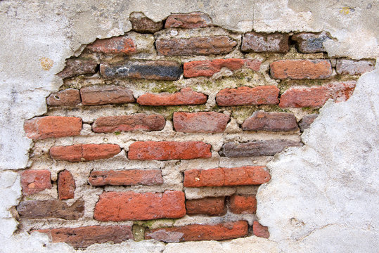 Old Brick Wall Covered In Concrete, Weather Worn Concrete Layer Has Crumbled Away Revealing Underlying Brick. Decrepit Condition.