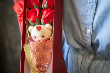 Florist's work: A girl demonstrates a box with a bouquet of red roses and a teddy bear.
