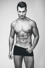 Fototapeta premium Portrait of handsome young man with stylish haircut in white underwear posing over gray background. Perfect hair & skin. Close up. Studio shot