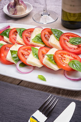 Caprese salad on a blue plate with an ornament on a light table in a restaurant.