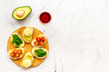 Healthy snacks. Set of toasts with vegetables like avocado, guacamole, rocket, cherry tomatoes on white stone background top view space for text