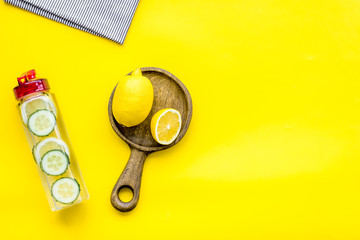 Make detox fruit water. Slices of lemon and cucumber in bottle on yellow background top view copy space