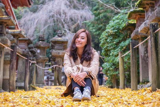 Portrait  image of a beautiful asian woman sitting on the ground among yellow colors tree leaves in autumn
