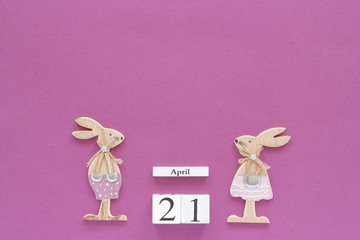 Wooden cubes calendar April 21 and pair of wooden easter bunnies on purple paper background. Concept Catholic Easter Copy space Template for lettering, text or your design Creative Top View.
