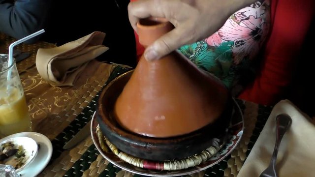 Moroccan cafe waiter brought fish tagine or tajine for a woman customer, then lifted cone shape lid. In the clay plate were vegetables and piece of fish in gravy; shaky table,handheld camera