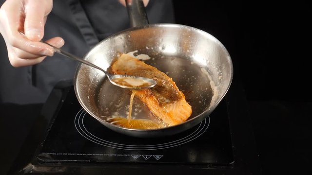 Food concept. Pan-fried Salmon, trout. Salmon fillet skin side down on the pan. Slices of red fish fried in a pan. Chef pouring oil with a spoon. hd . Slow motion.