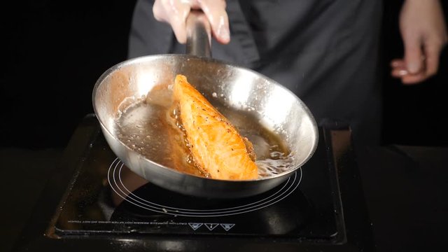 Unhealthy fat food concept. Pan-fried Salmon, trout. Salmon fillet skin side down on the pan. Slices of red fish fried in a pan. Chef pouring oil with a spoon. hd . Slow motion.