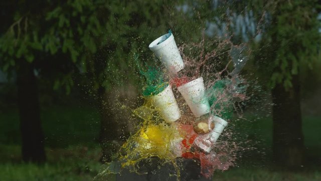 Potato gun shooting stack of cups with colorful liquids in super slow motion