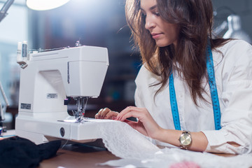 Cropped image of female tailor stitching fine lace with sewing machine sitting in dressmaking studio