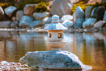 Japanese lantern statues isolated on a rock in the middle of a pond