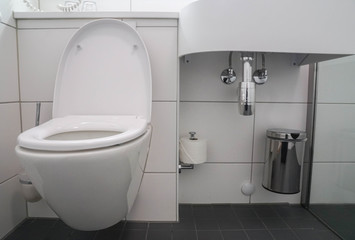 modern bathroom interior of white ceramic toilet bowl and washbasin sink with stainless bin for trash