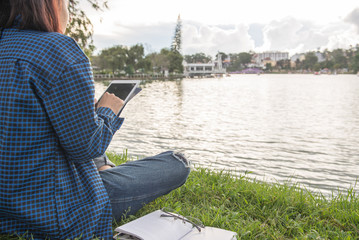 Close-up of woman tapping on tablet screen, sitting at a lake