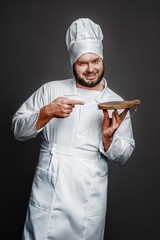 Bearded overweight man in chef uniform smiling and looking at camera while standing on black...