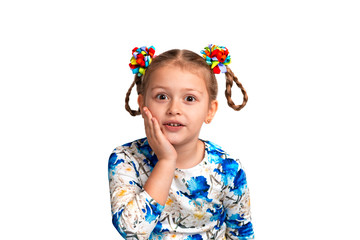 Studio waist up portrait of a little girl wearing shirt with a print and with two pigtails and color bows on a gray background. She is holding her cheek with her palm and is surprised at something